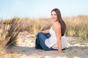 A person in casual attire lying on a sandy beach at sunset with dunes and grass in the background.