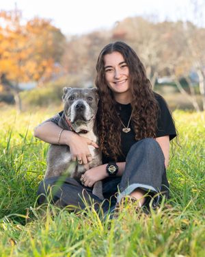 A person and their gray dog lay together in a grassy field during autumn.