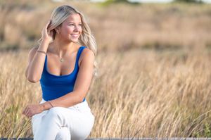 A woman in a blue tank top walks through a golden field of tall grass at sunset.