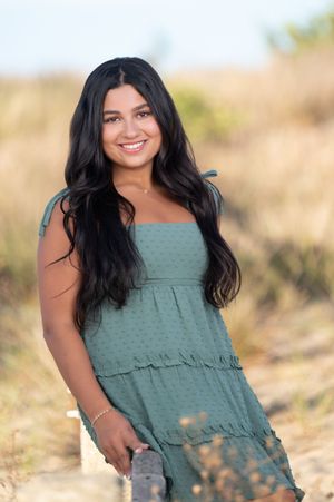 Portrait of someone wearing a sage green tiered sundress with long dark hair outdoors in a natural setting.