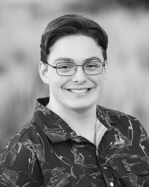 Black and white portrait photo of someone wearing glasses and a patterned shirt, smiling warmly at the camera.