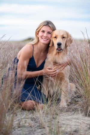 Golden retriever and companion posing together in tall beach grass during outdoor photo session at sunset.