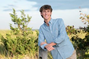 A person in a light blue button-down shirt poses outdoors against a natural backdrop during golden hour.
