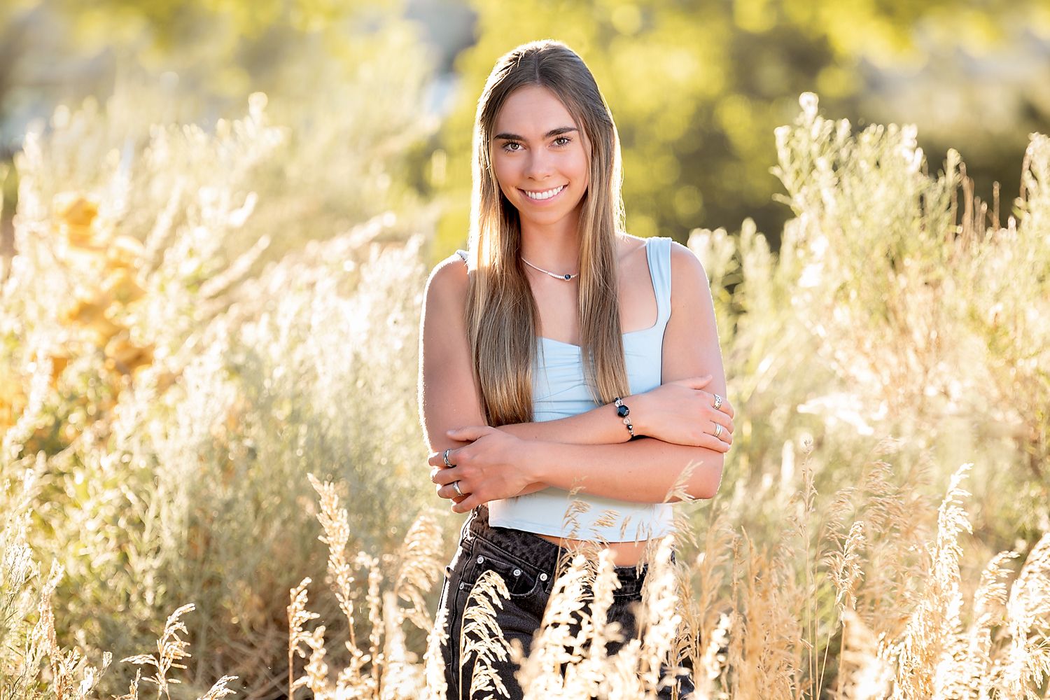 A person in a blue tank top sits among tall golden grass during a sunny outdoor photo session.