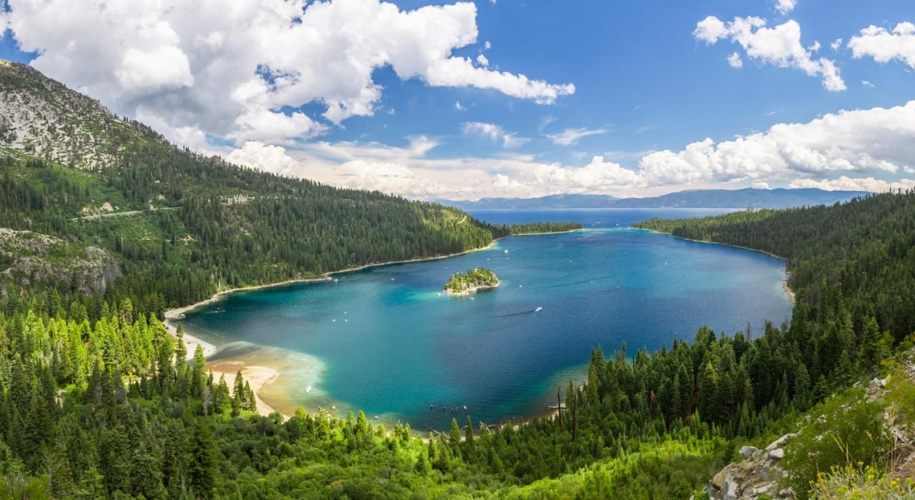 Panoramic aerial view of turquoise Emerald Bay at Lake Tahoe surrounded by pine forests.