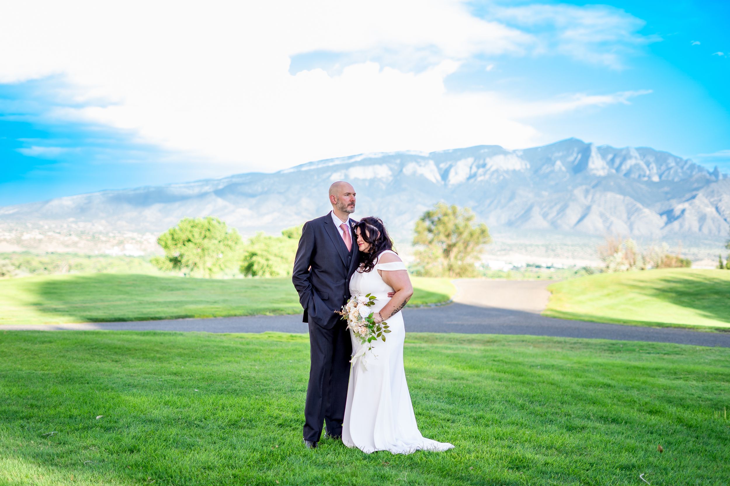 A couple poses for their wedding photo on a golf course with mountains in the background.