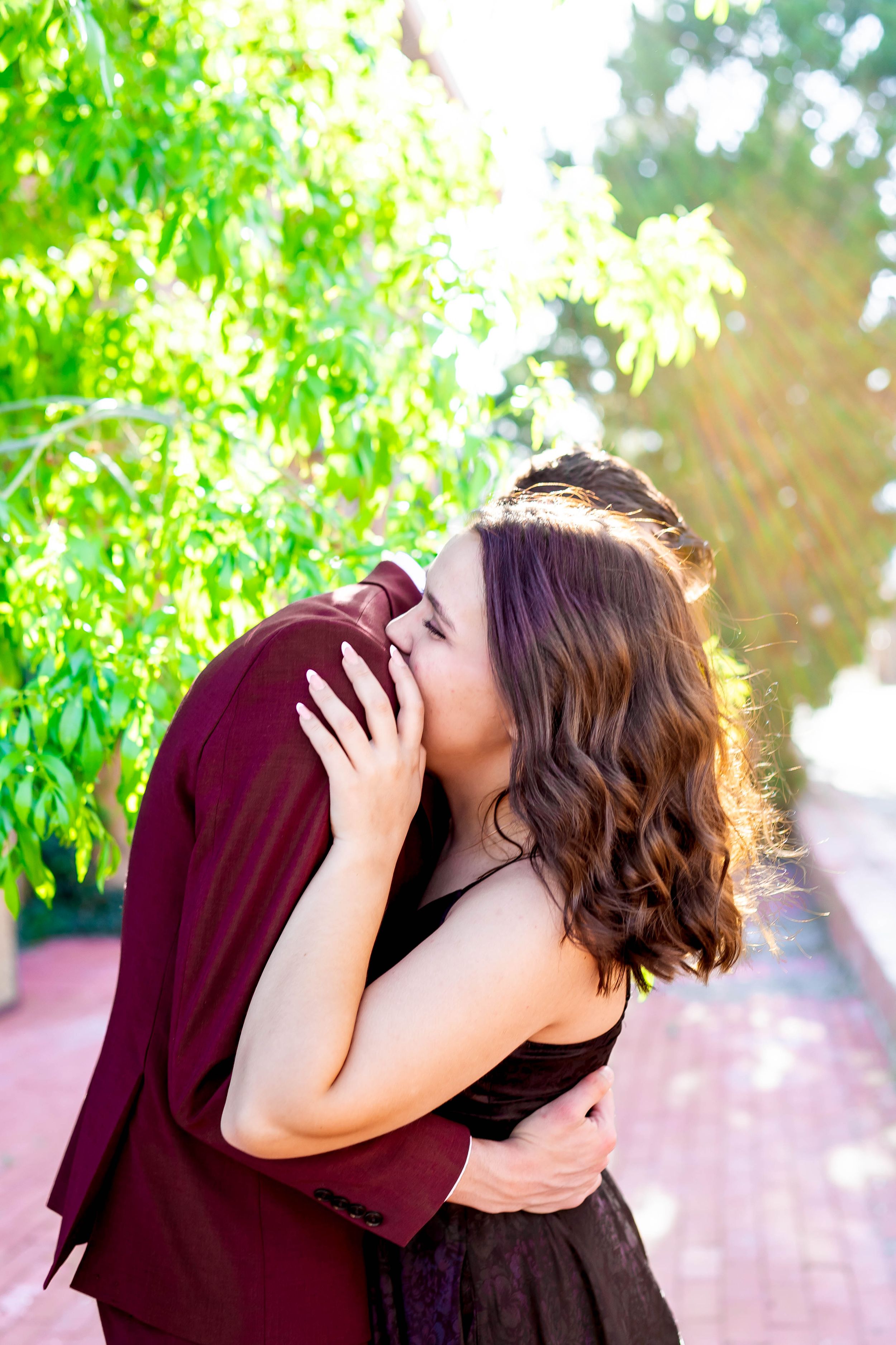 A romantic couple embracing in a sunlit garden setting with lush green foliage.