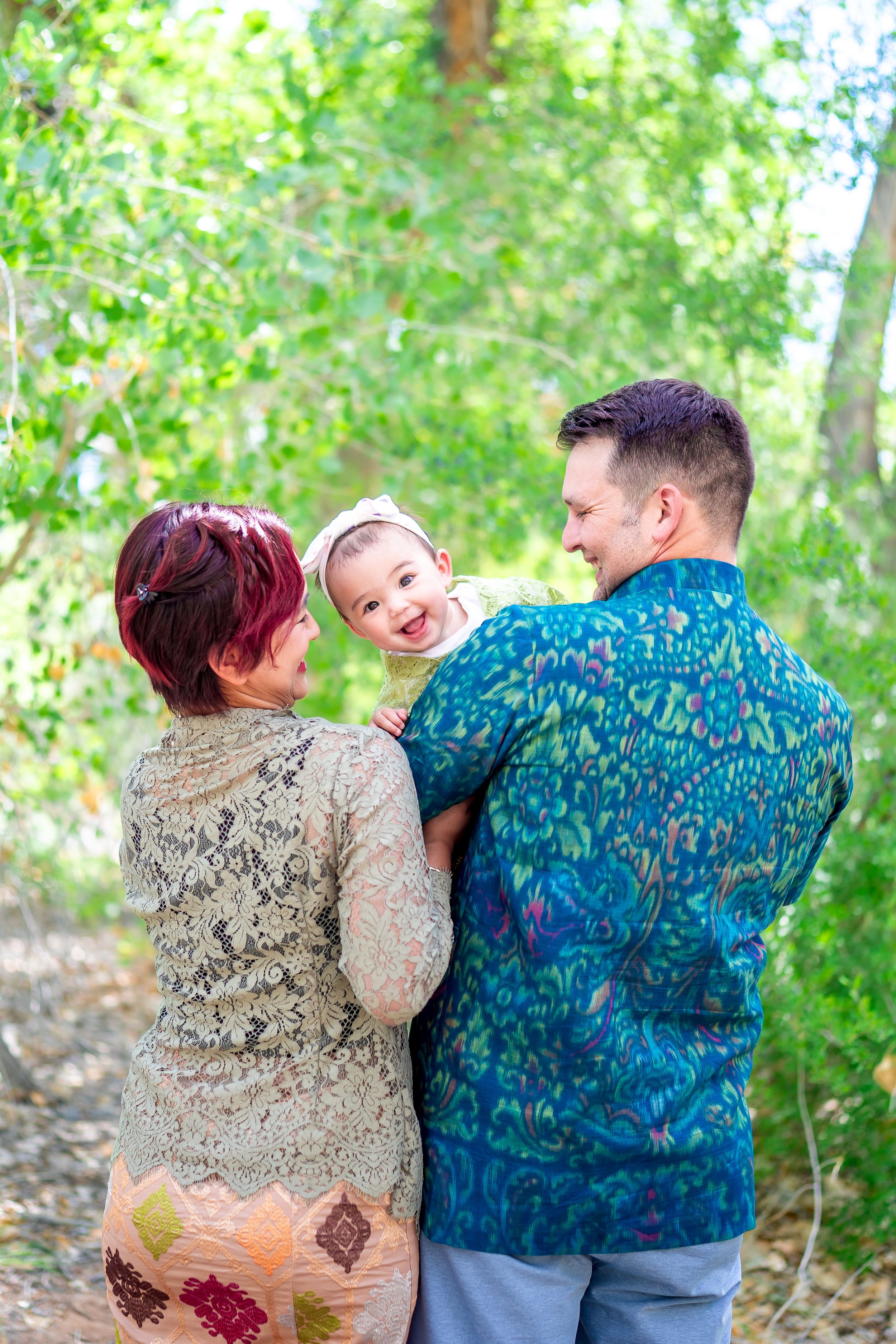 Three people sharing a joyful moment together outdoors surrounded by green trees.