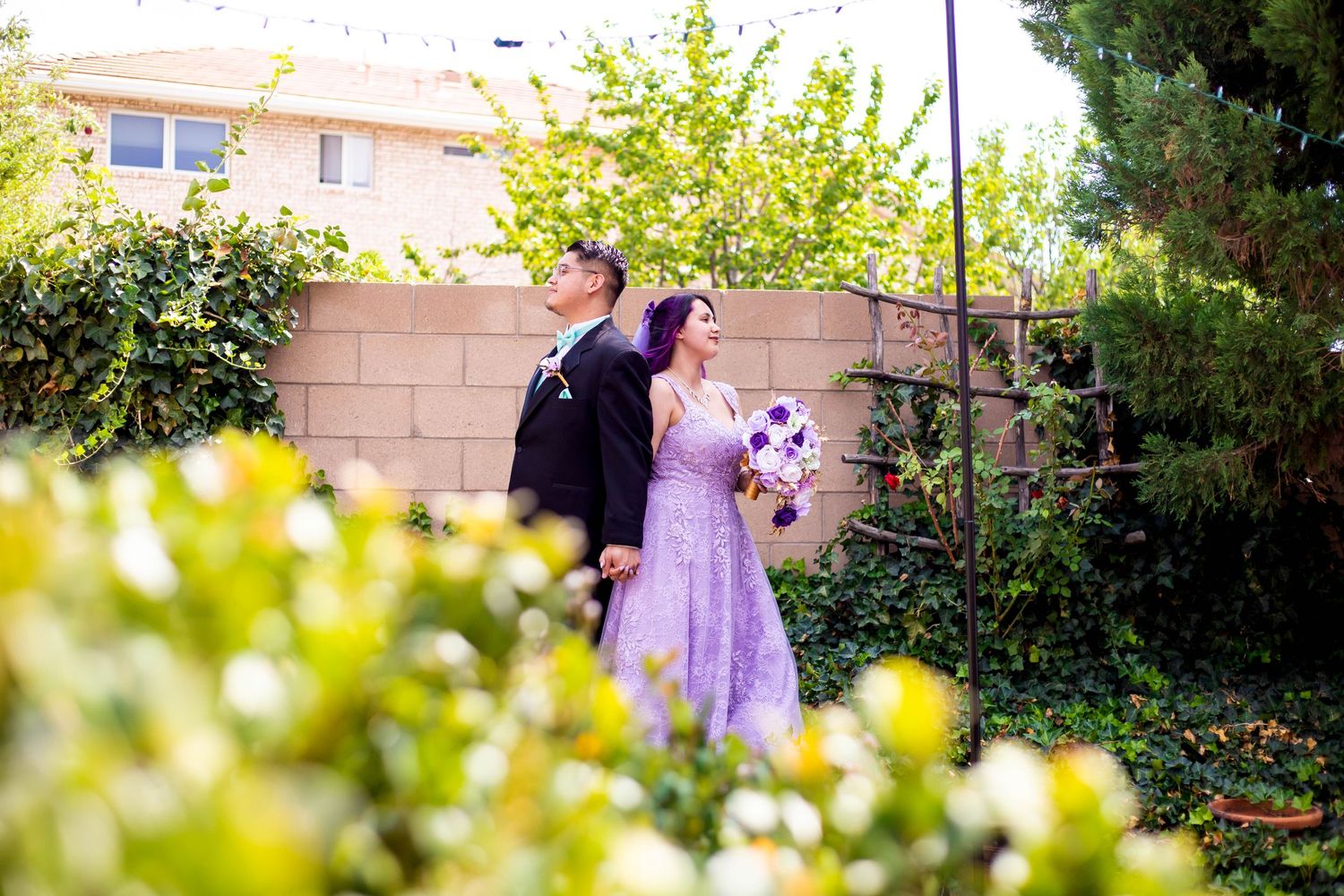 Wedding couple shares intimate moment in garden setting with soft bokeh effect.