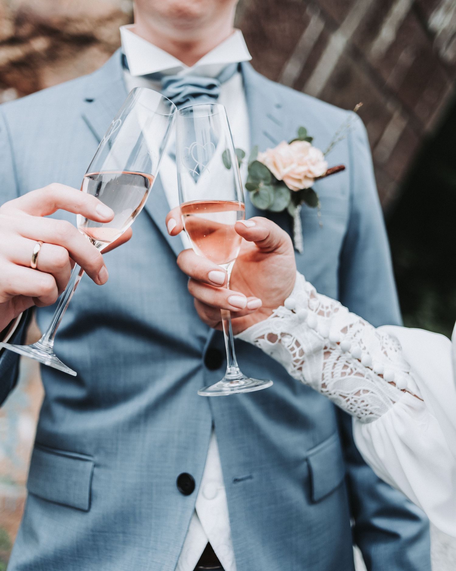 Wedding toast with champagne glasses showing groom's blue suit and bride's lace sleeve.