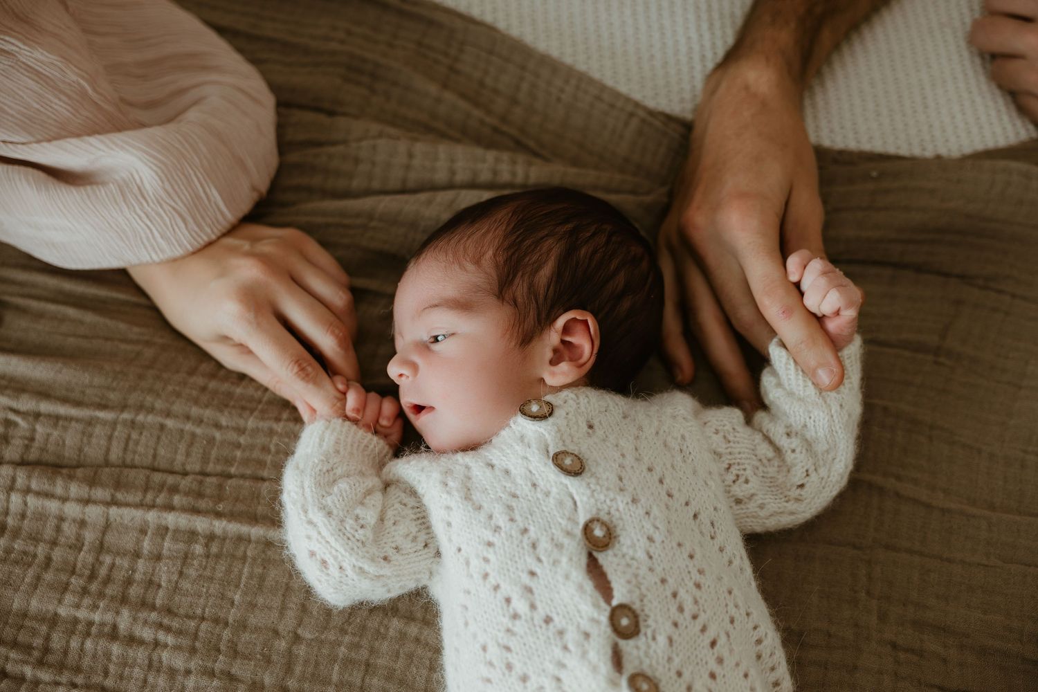 Bebé recién nacido dormido en una cesta de mimbre con rosas rosa y burdeos, mientras su mamá lo mira cerca. Sesión newborn en Valencia