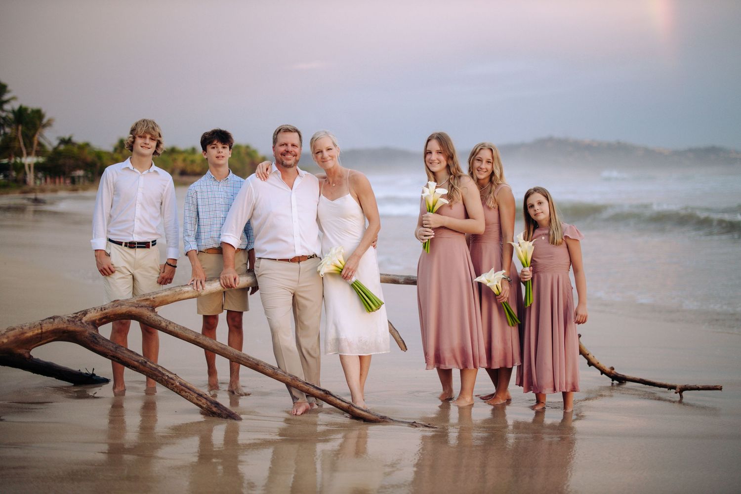 Family group posing on driftwood at beach during sunset photo session.