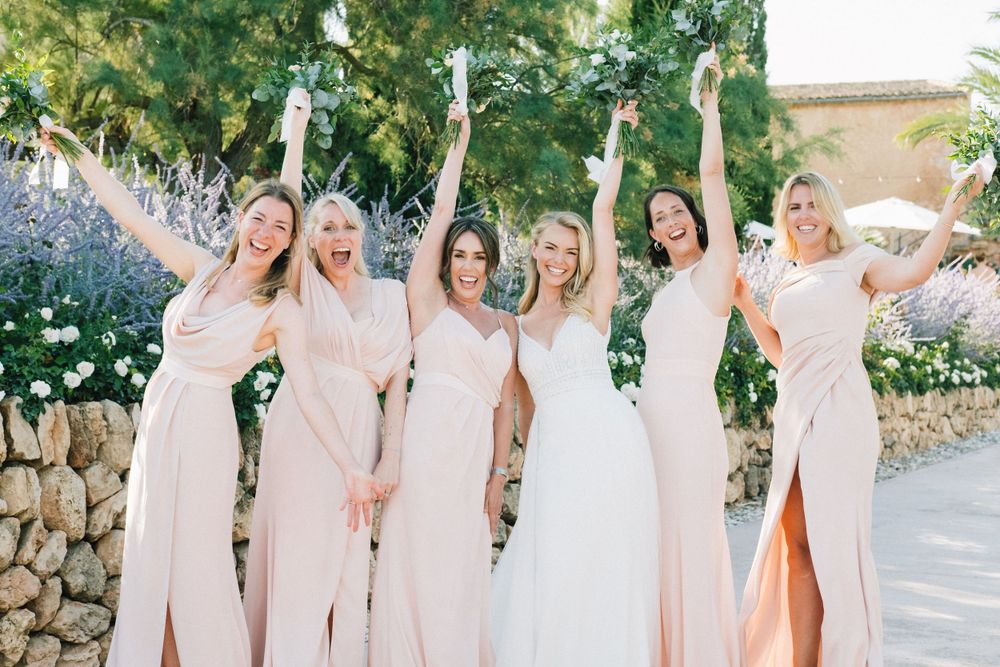 Joyful bridesmaids in blush dresses celebrating with bride in garden setting.