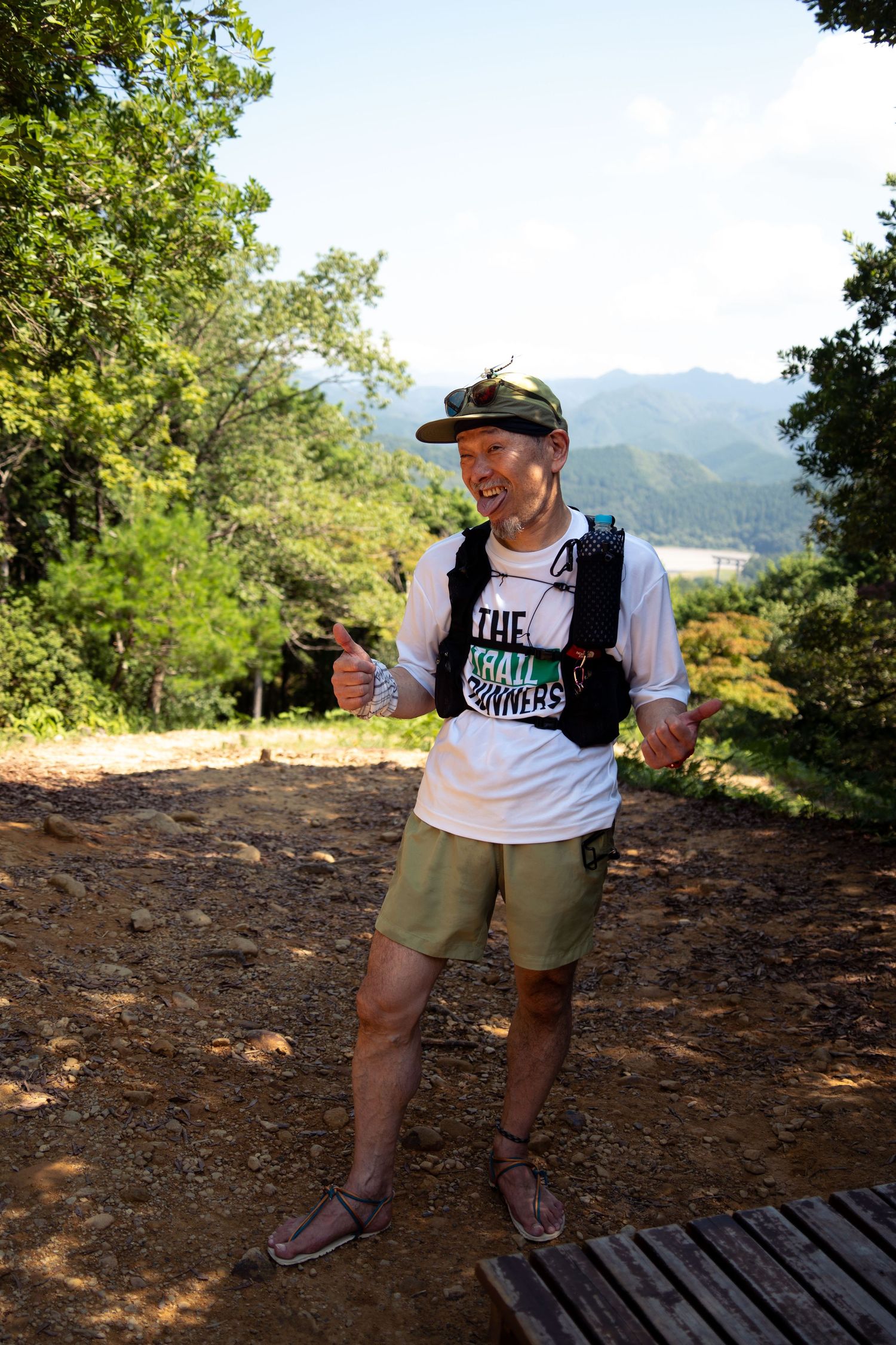 Person hiking on a dirt trail with mountains and trees in the background.