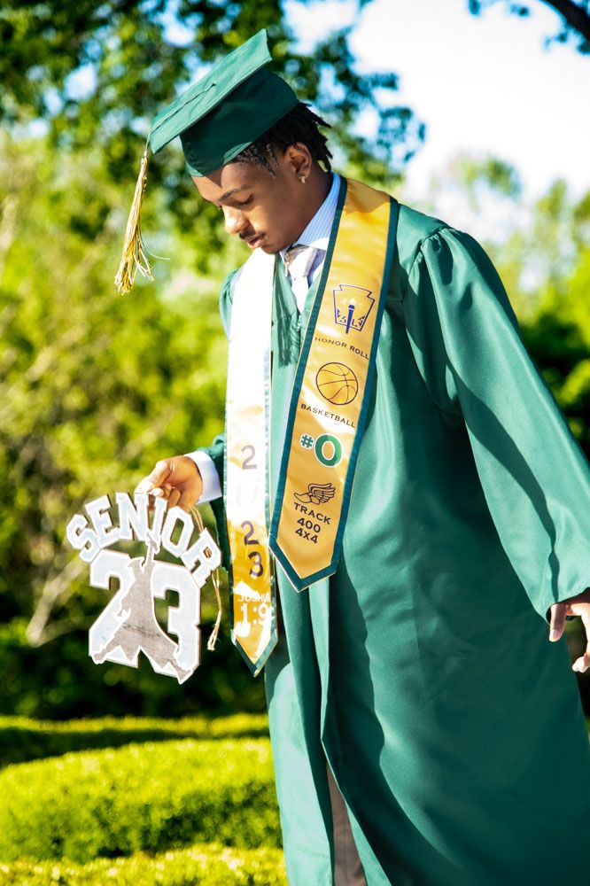 Green graduation gown with gold honor stole and white 2023 senior sash displayed outdoors.