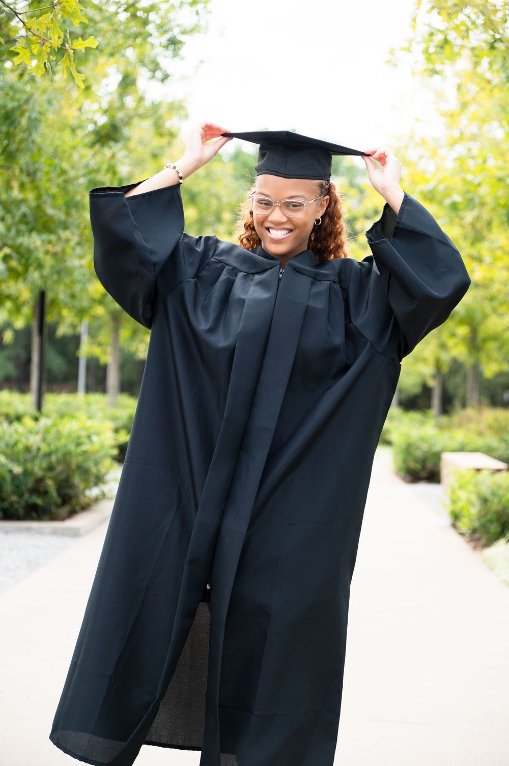 Graduate in black cap and gown celebrates with energetic poses in a sunny outdoor setting.