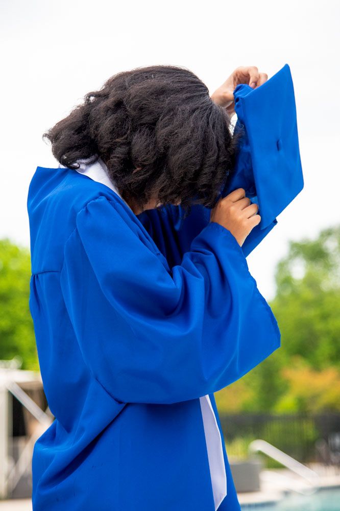 Graduate in bright blue graduation gown adjusts cap during outdoor photo session.