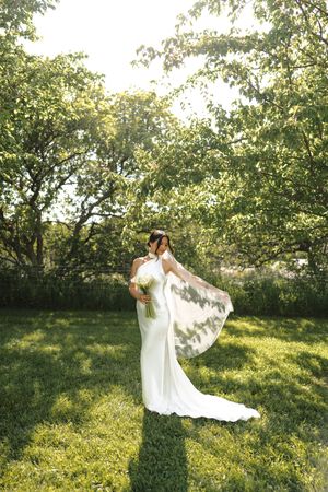 A bride in a flowing white dress twirls gracefully in a sunlit orchard during a golden hour photo session.