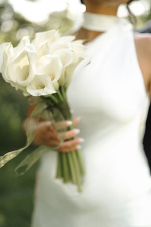 Elegant white calla lily bouquet held against a wedding dress in soft focus.