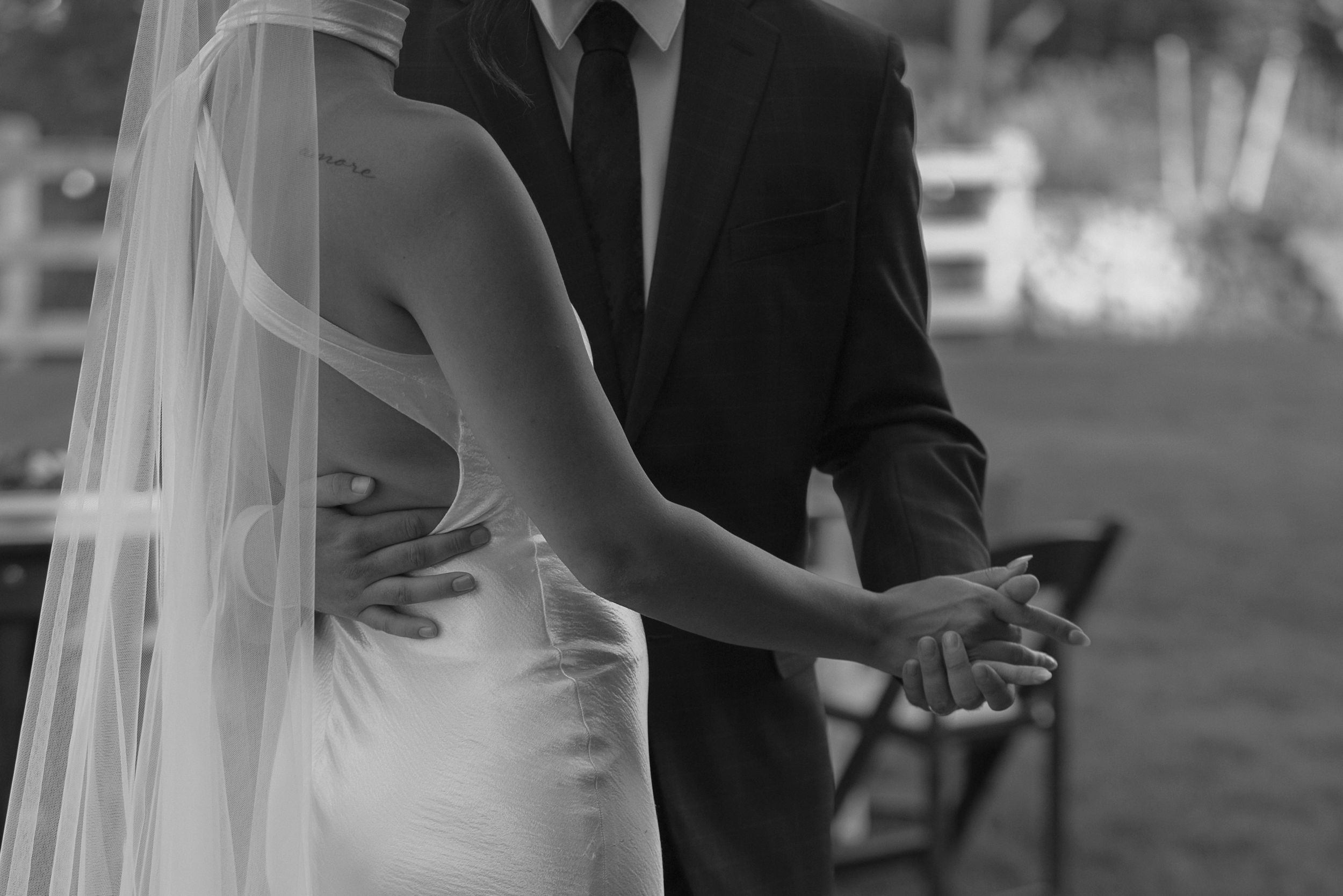 A bride and groom share a tender moment under a flowing veil during their outdoor wedding ceremony.