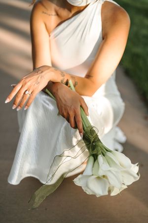 Close-up shot of hands smoothing out details on a white wedding dress against a soft blurred background.