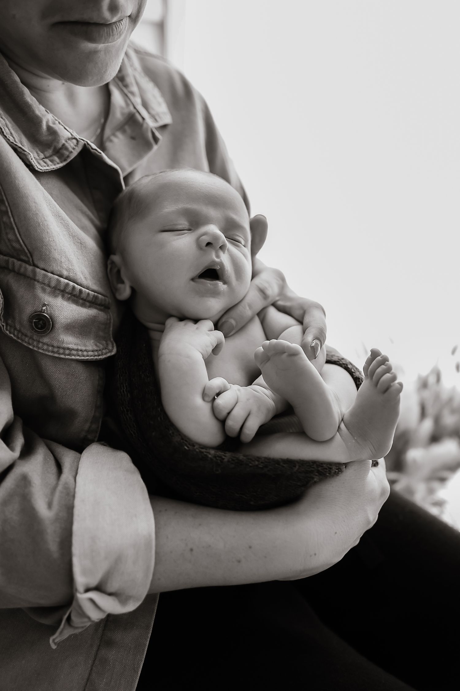 Sleeping newborn baby rests peacefully on parent's chest in black and white portrait.