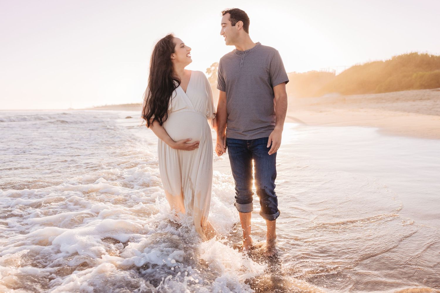 Couple splashing in ocean waves during sunset beach photography session.