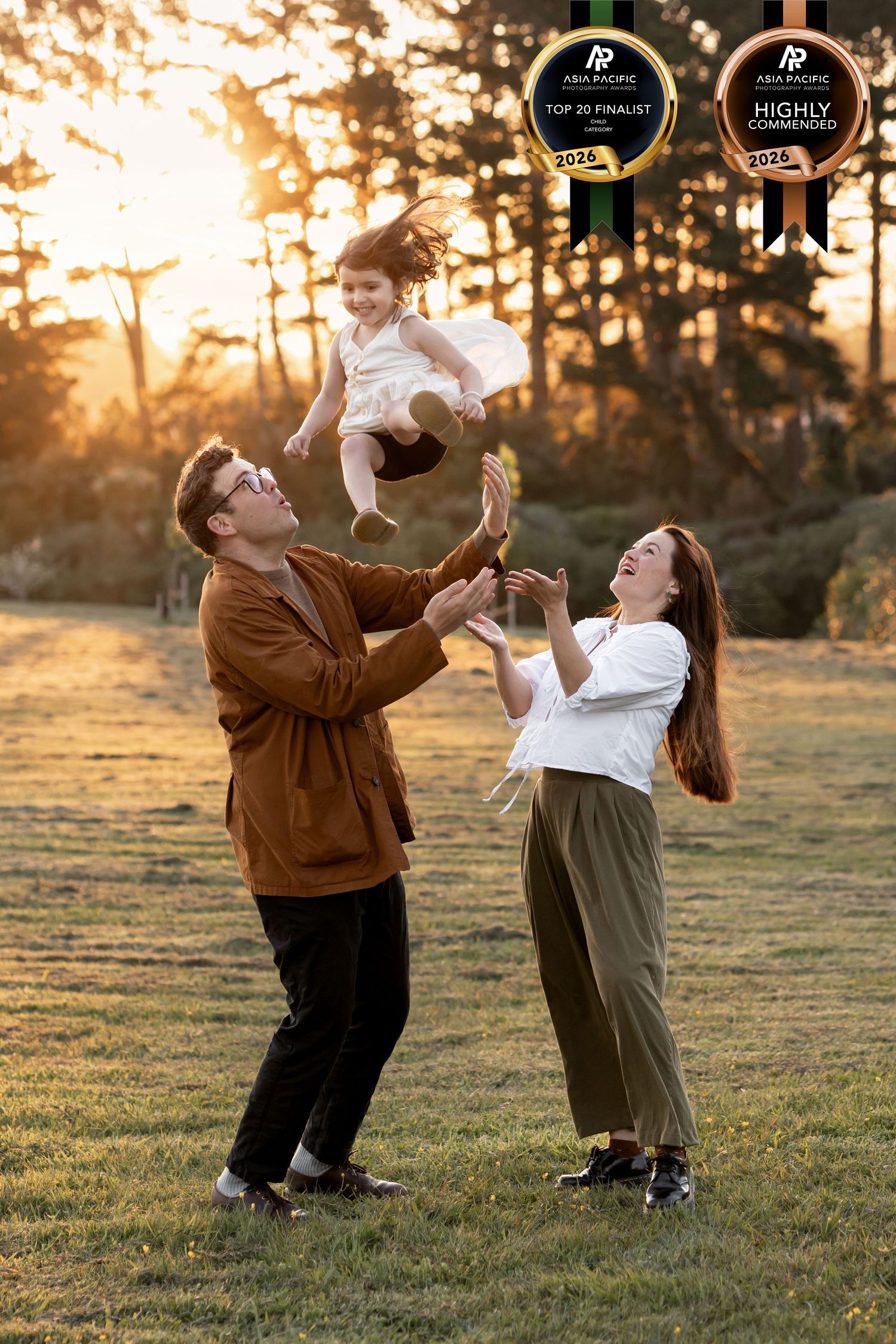 Playful family portrait of Toddler being thrown into the air while the parents lovingly look up at her and have hands held out. Golden hour