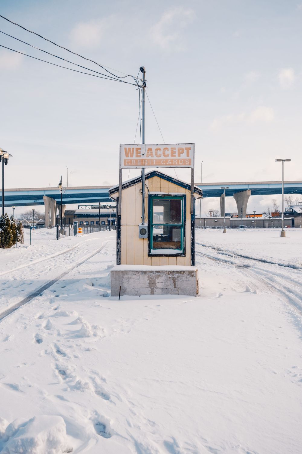 A small ticket booth covered in snow with power lines and industrial buildings in the background.