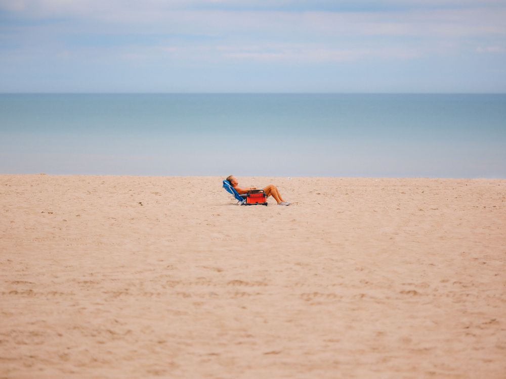Lone beach chair on empty sandy shore against calm ocean horizon.