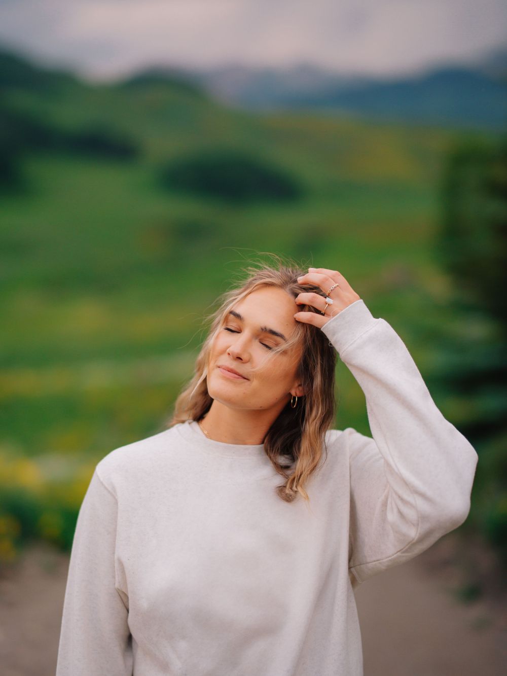 Person in white sweater with peaceful expression against rolling green hills.
