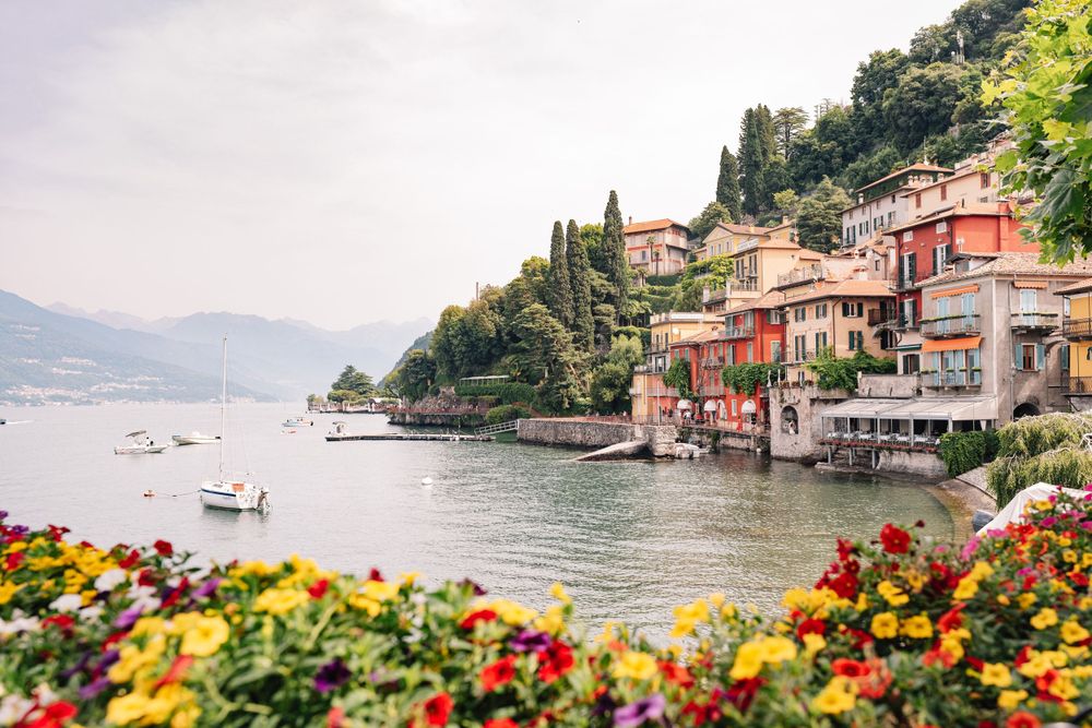 Colorful flowers frame a view of Lake Como with traditional Italian villas along the waterfront.
