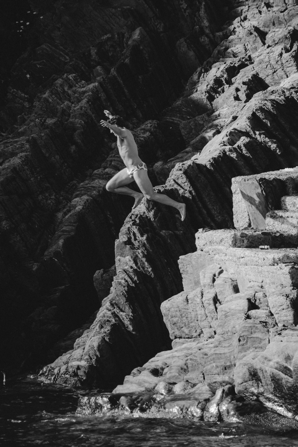 Black and white photo of a cliff diver leaping from rocky heights into water below.