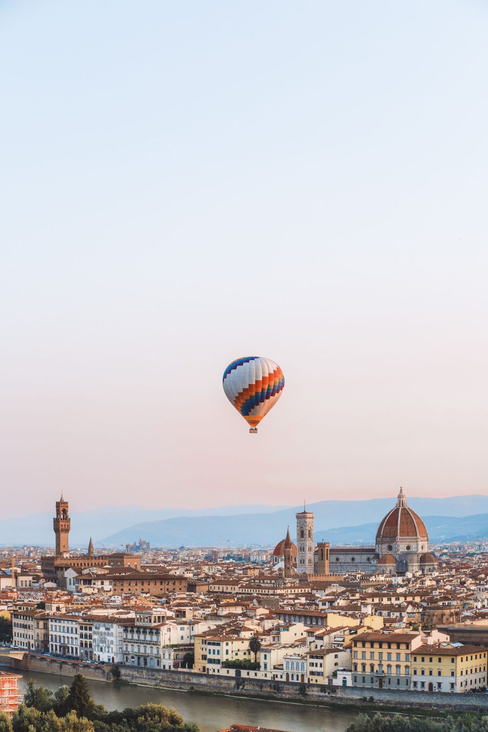 Hot air balloon floating over Florence's iconic skyline with the Duomo cathedral at sunset.