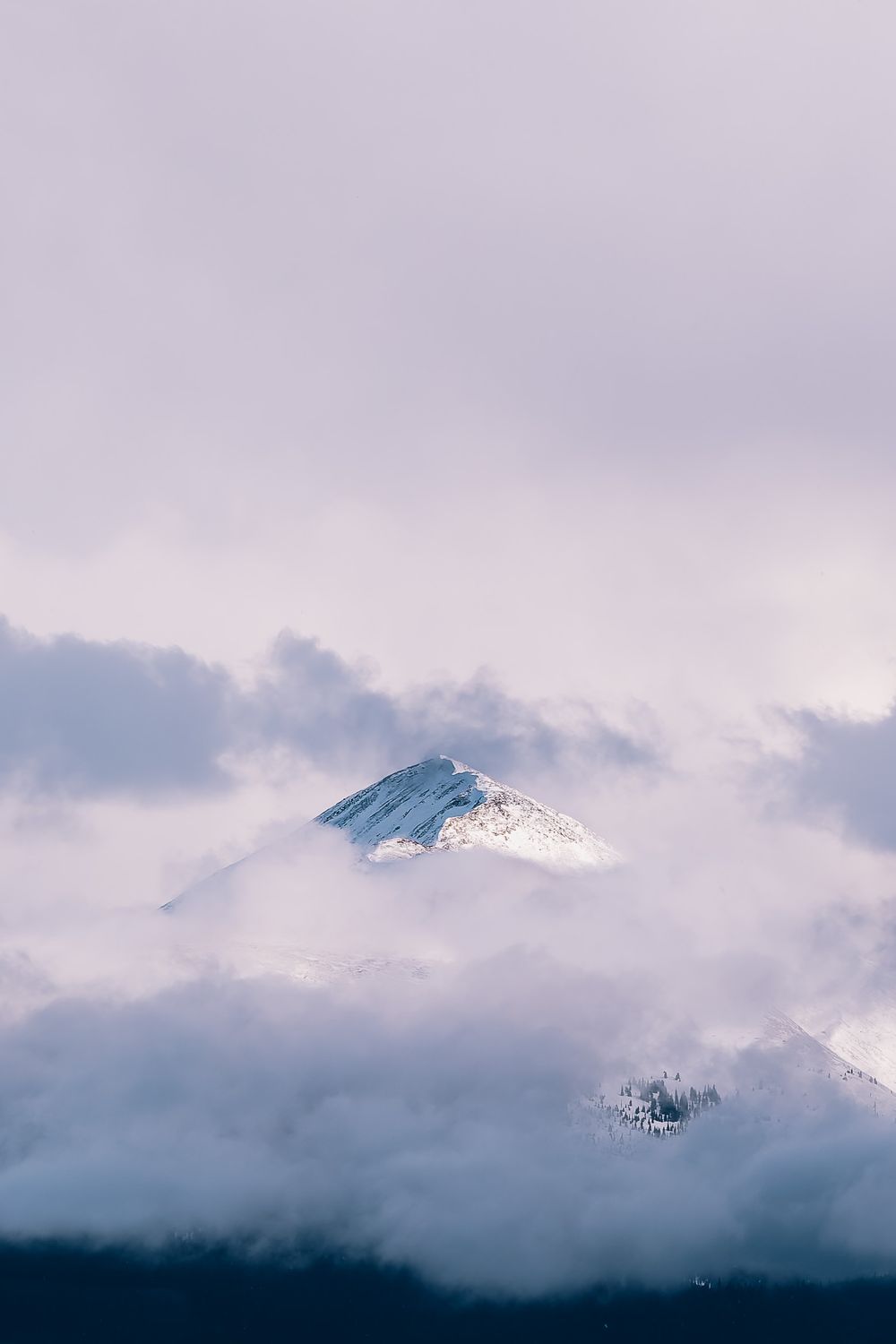Snow-capped mountain peak emerging through misty clouds in soft purple light.