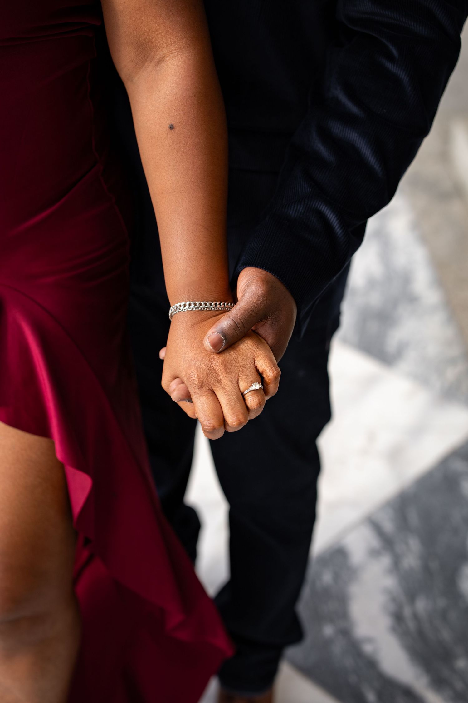 Close-up of two people holding hands, one wearing red fabric and one in dark clothing with a bracelet visible.