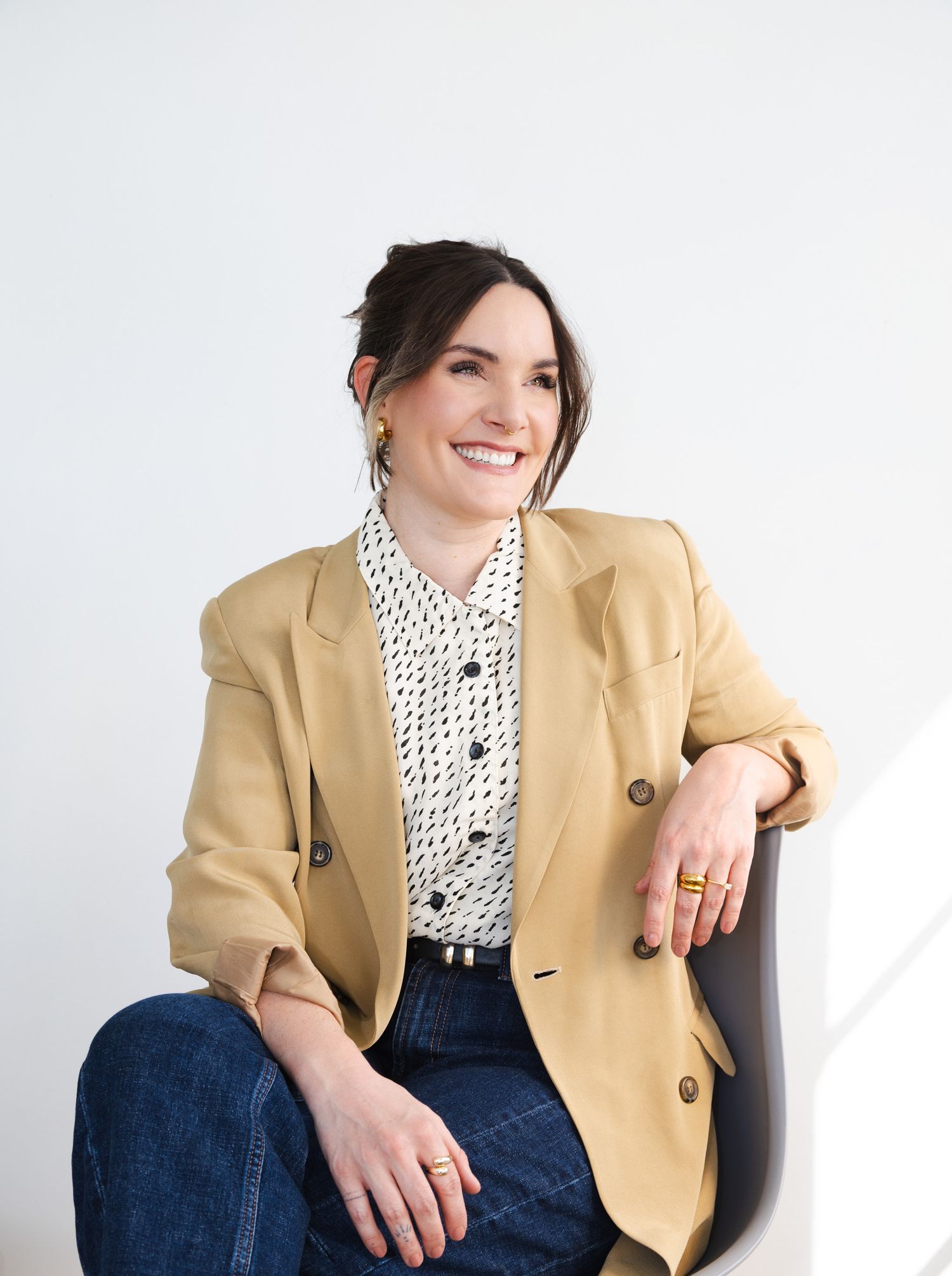Professional portrait of someone wearing a polka dot blouse and tan blazer sitting casually against a light background.