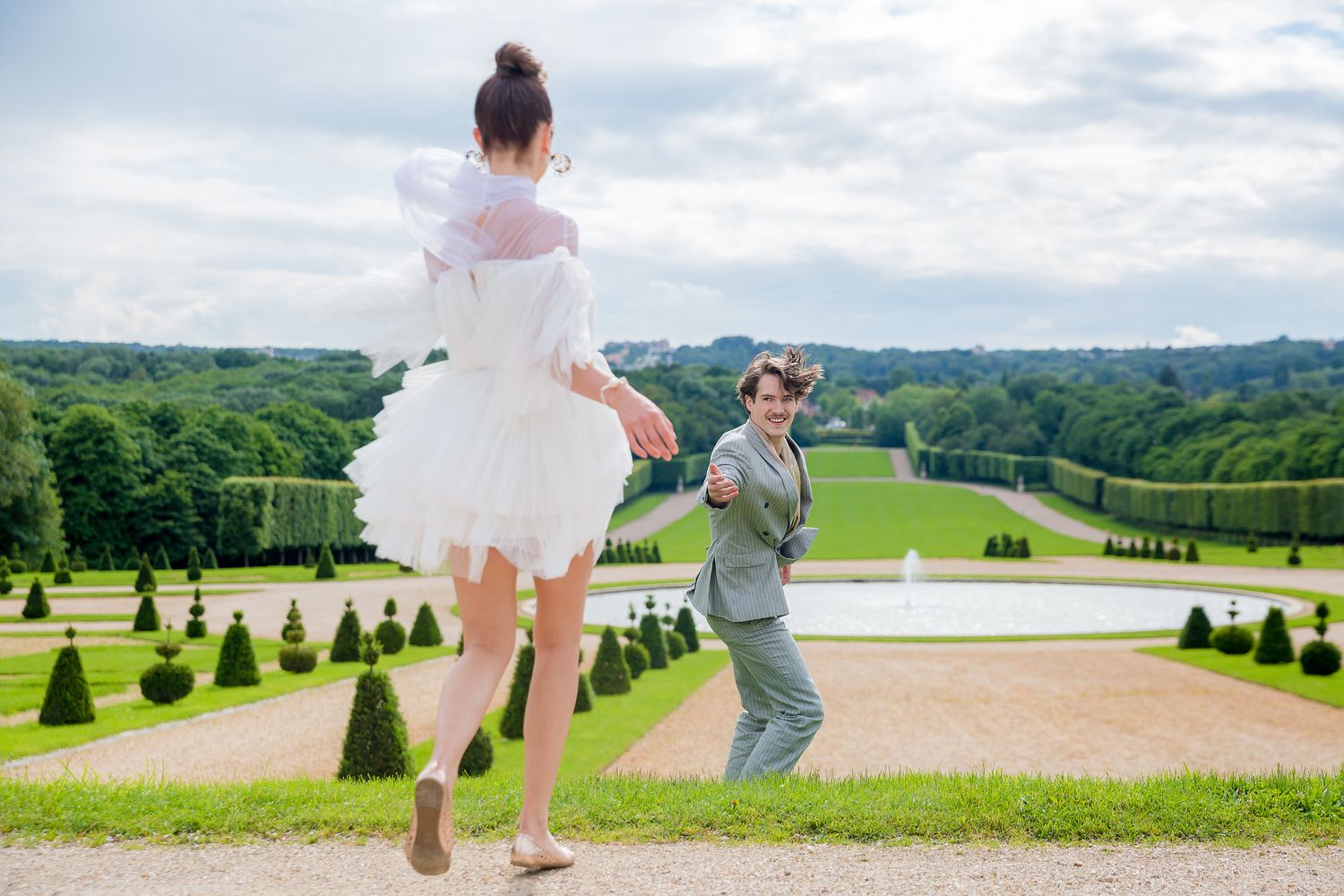 Couple poses playfully on grand estate grounds with manicured gardens in background.