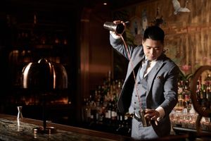 Bartender pouring cocktail in classic bar setting.