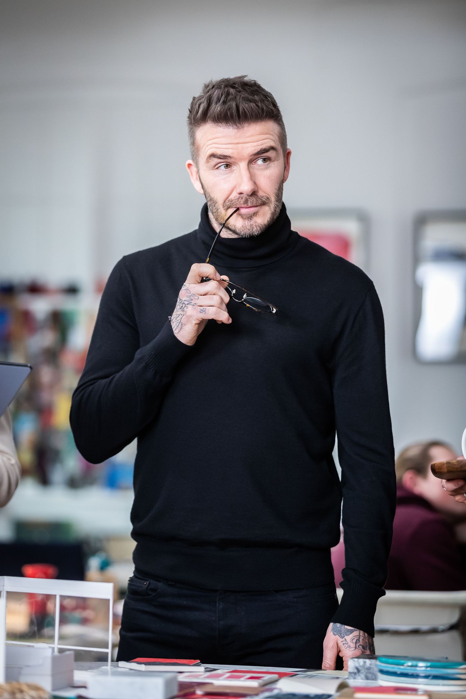 Person in black sweater gestures while sitting at desk in office setting.
