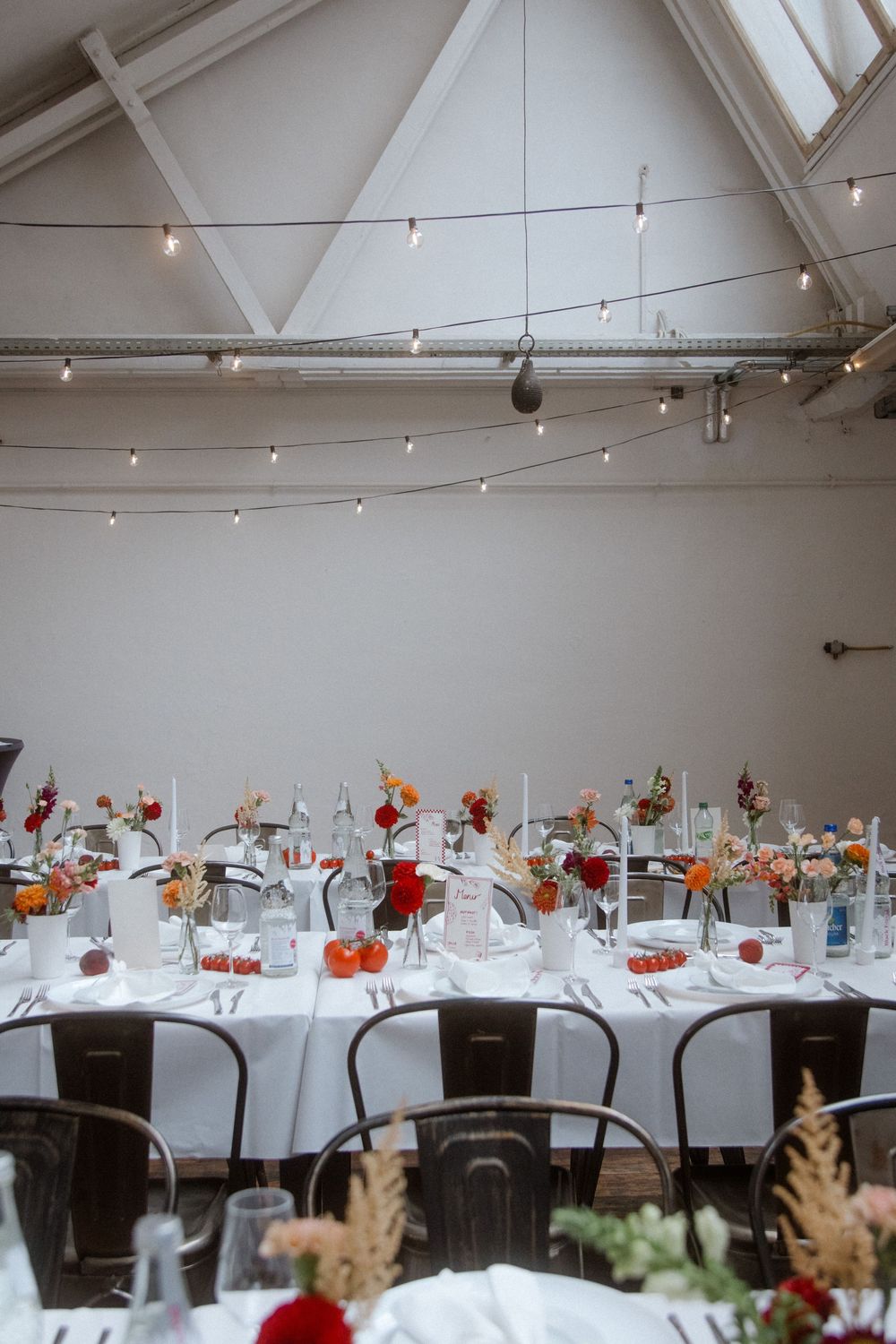 Modern wedding reception venue with elegant white tables and colorful floral centerpieces set against crisp gallery walls.