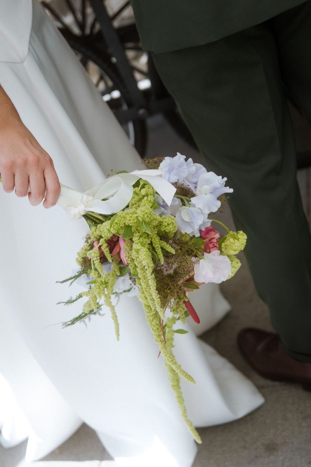 A delicate floral arrangement with purple blossoms and green ferns resting against a white surface.