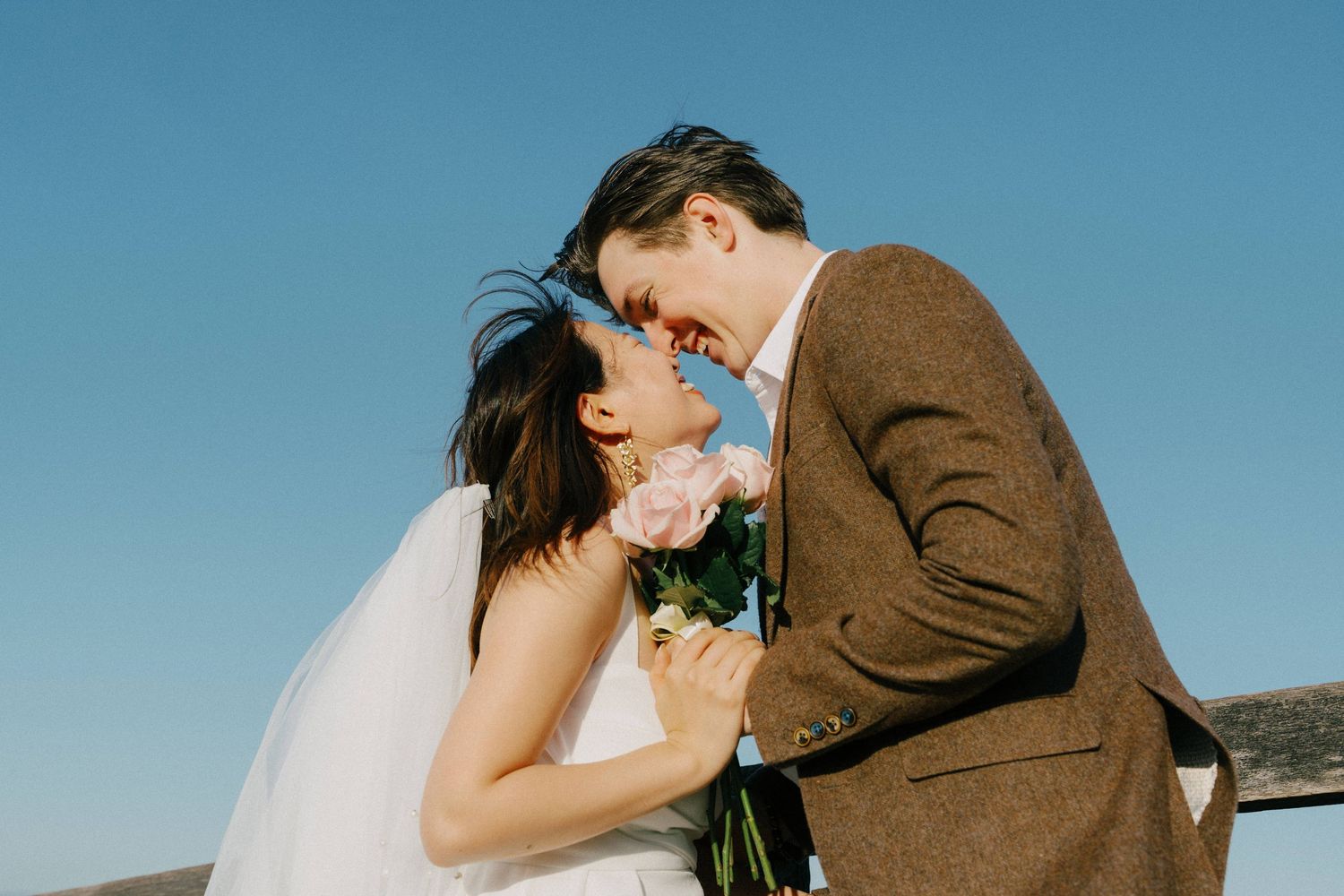A tender romantic photo of a couple sharing a close moment against a blue sky on their wedding day.