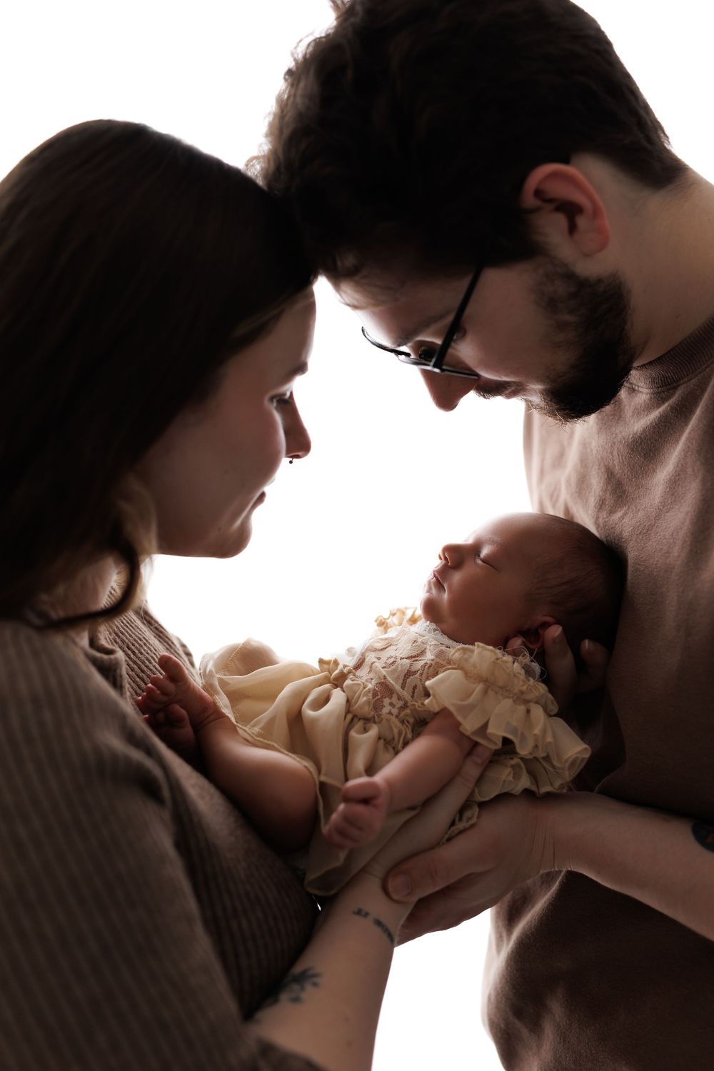 New parents lovingly gaze at their sleeping newborn baby, captured in a beautiful backlit portrait.