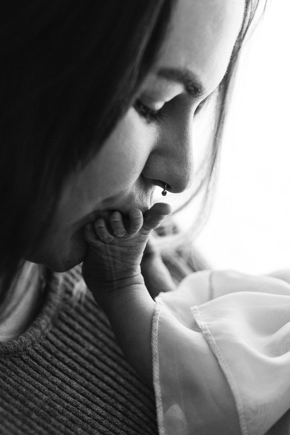 Black and white photo of a mother tenderly kissing her newborn baby's tiny hand in a heartfelt moment.