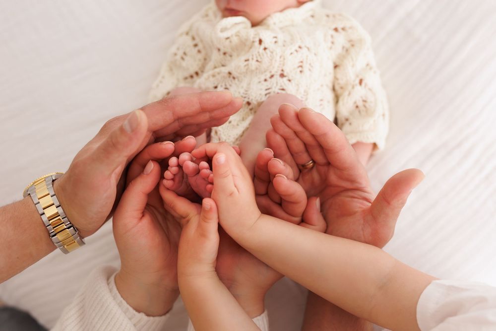 Family hands cradling newborn baby feet in a tender and loving close-up photo.
