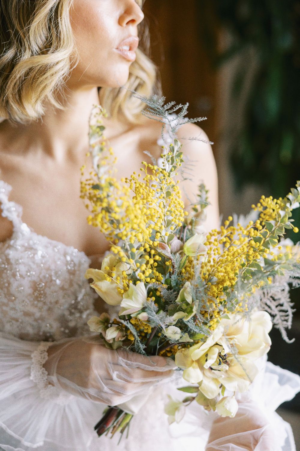 Close-up portrait of a bride holding a delicate bouquet of yellow and cream wildflowers.