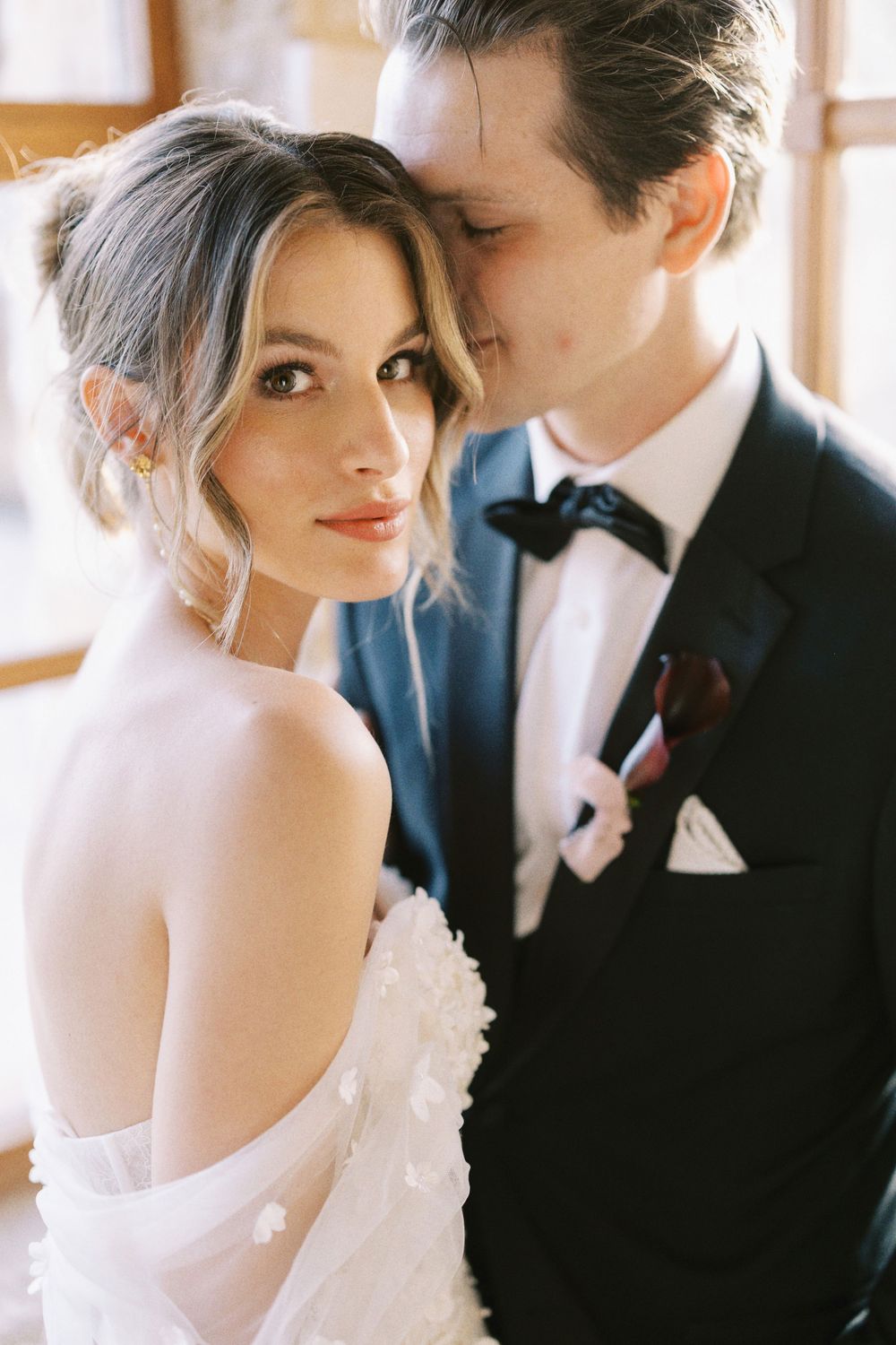 Close-up romantic wedding portrait of a stylish bride and groom in classic black-tie attire.