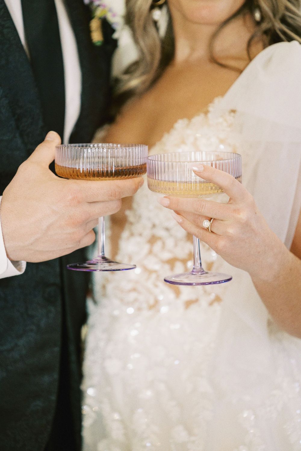 Detailed close-up of a bride and groom clinking champagne coup glasses in a toast.