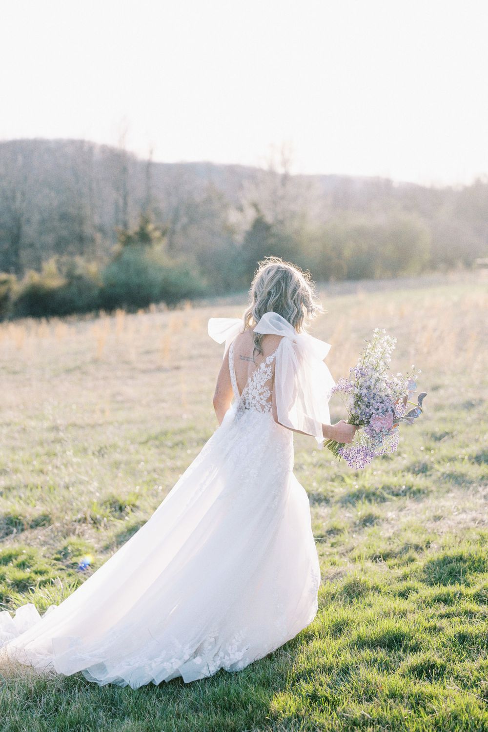 Bride walking away through a golden grassy field at sunset, holding her bouquet.